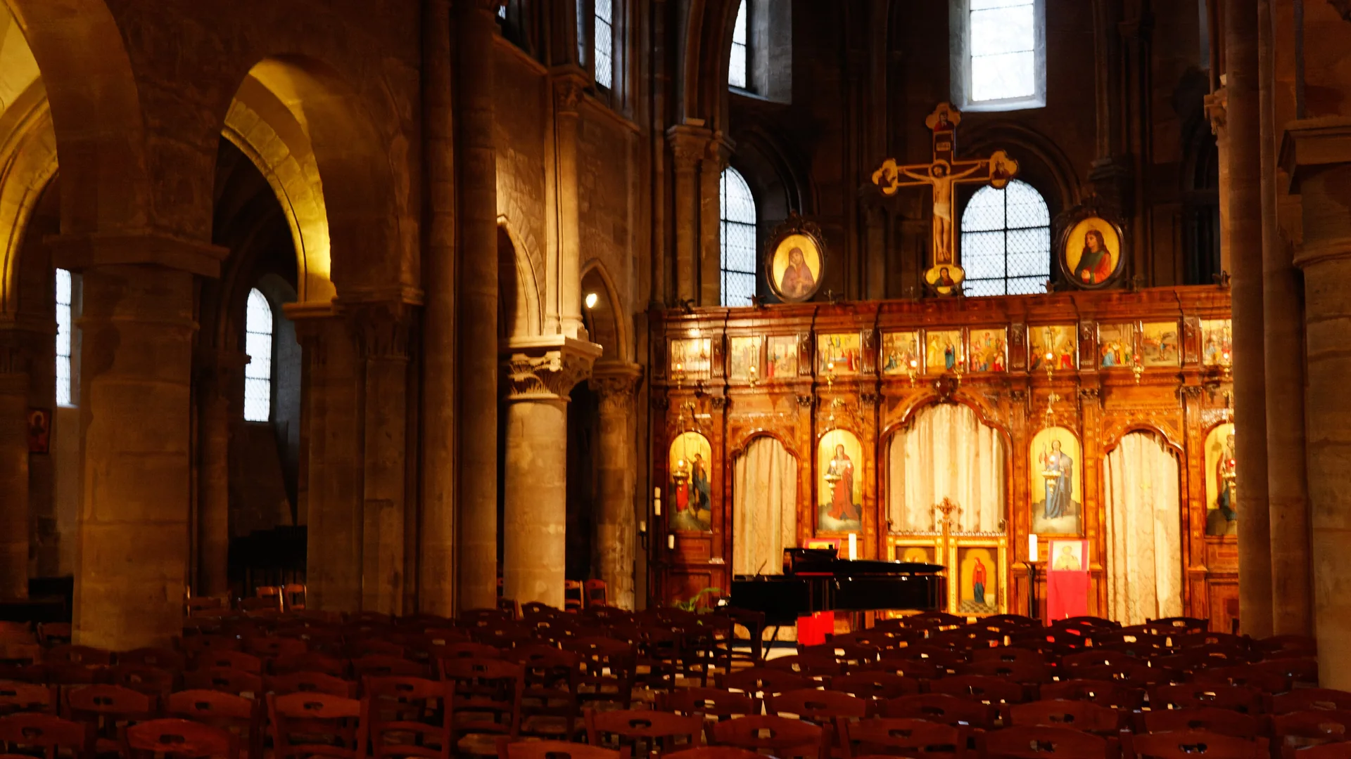 Řady dřevěných židlí a klavír před pozlaceným, ikonami pokrytým ikonostasem uvnitř kostela Saint-Julien-le-Pauvre v Paříži