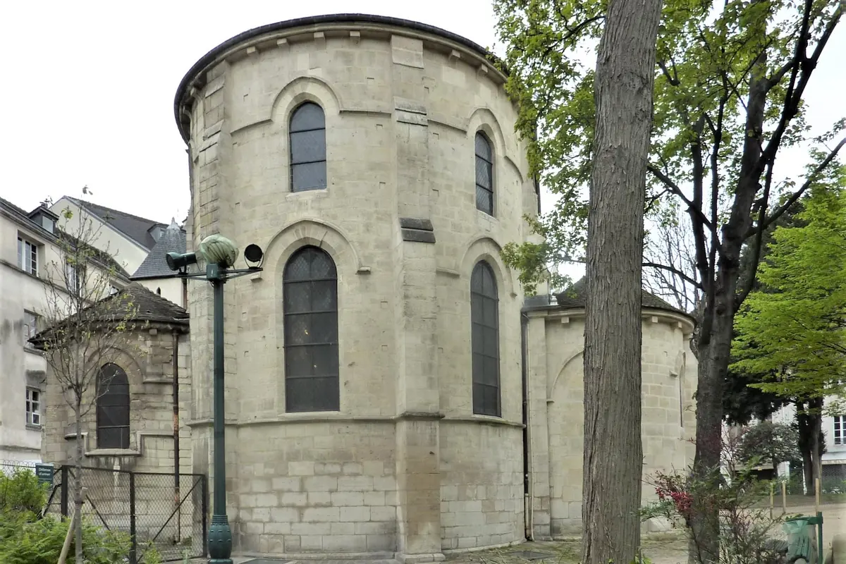 Zaoblený kamenný východní závěr kostela Saint-Julien-le-Pauvre s vysokými klenutými okny, orámovaný stromy.