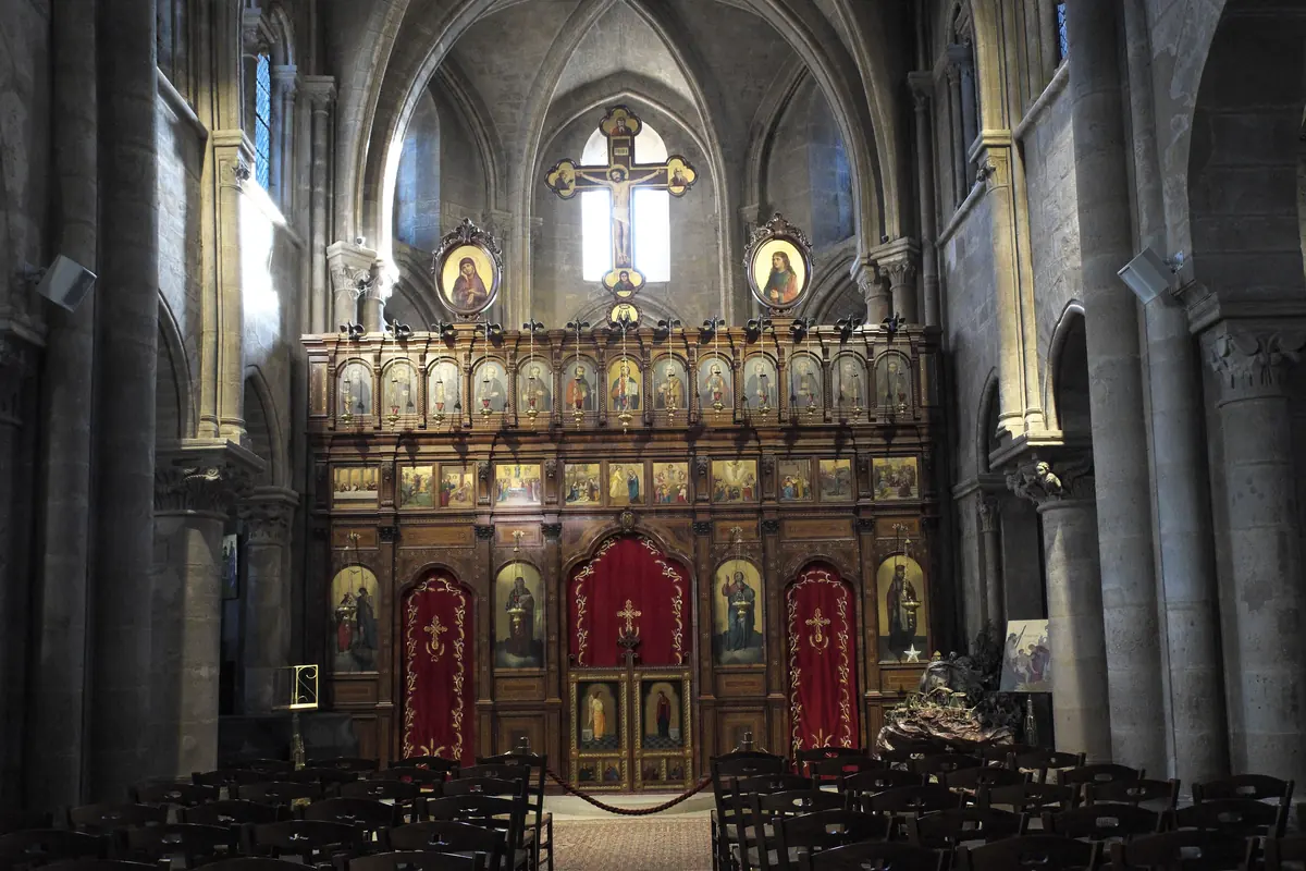 Vyřezávaný dřevěný ikonostas kostela Saint-Julien-le-Pauvre s řadami malovaných ikon a červenými závěsy mezi středověkými sloupy hlavní lodi.