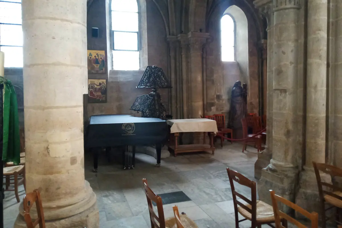 Klavír a řady dřevěných židlí vedle kulatého románského sloupu uvnitř kostela Saint-Julien-le-Pauvre.