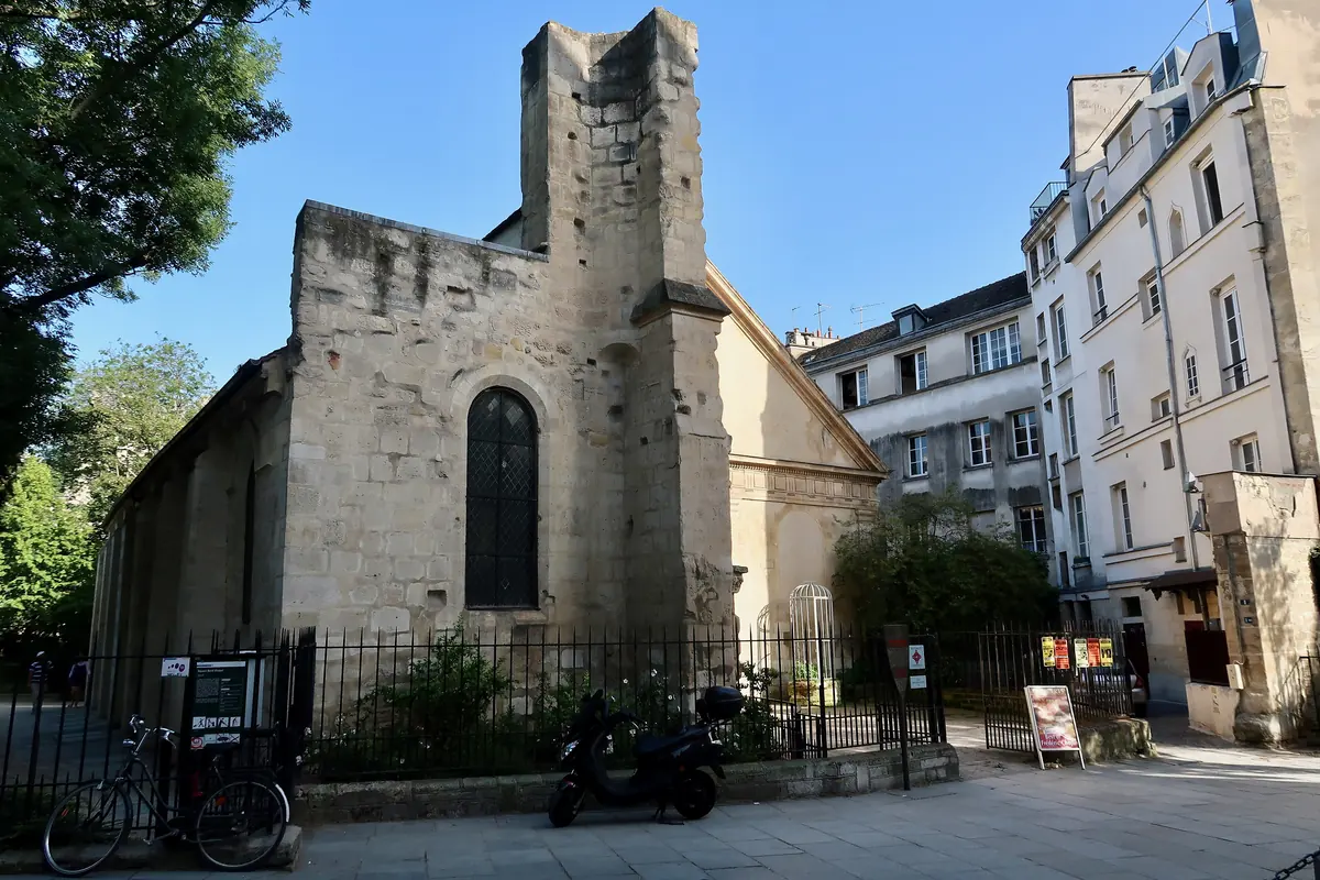 Krémově zbarvené kamenné západní průčelí a nedokončený pahýl věže kostela Saint-Julien-le-Pauvre pohledem z ulice, s pařížskými obytnými domy po boku.
