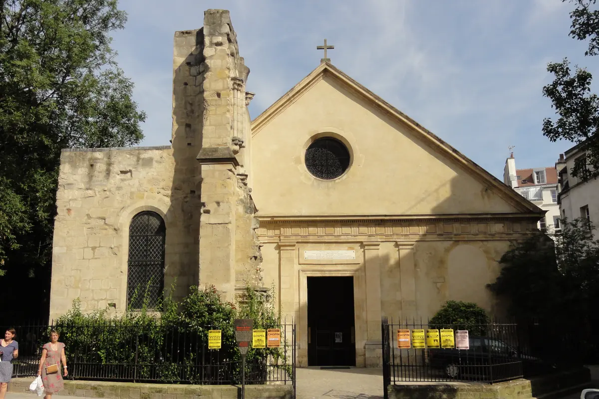Prostý krémový západní průčelí kostela Saint-Julien-le-Pauvre s kulatým oknem nad dveřmi a hrubým pahýlem nedokončené věže po jeho boku.